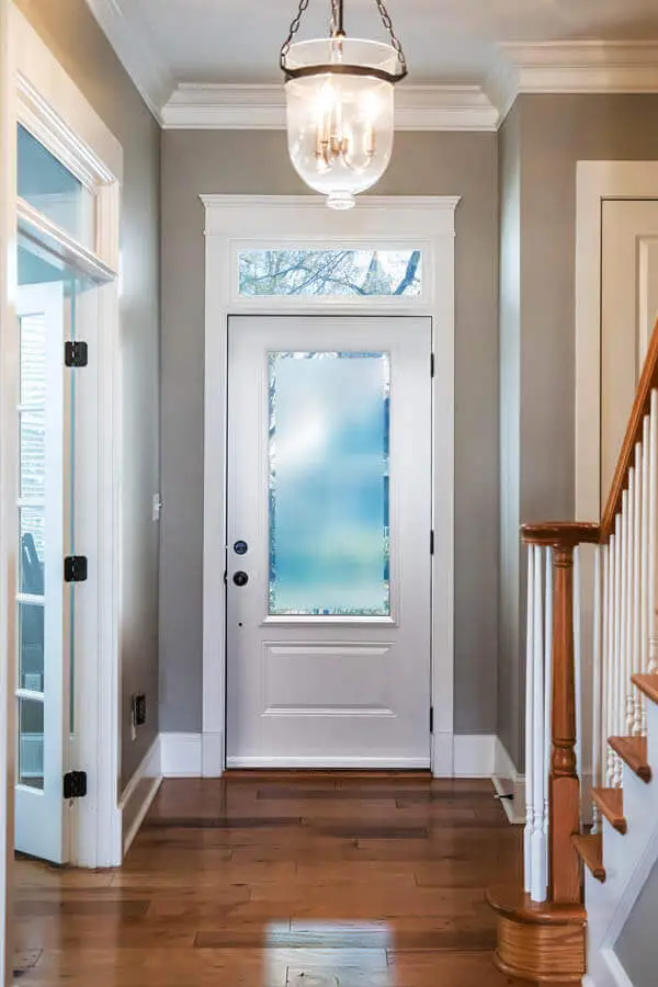 NTI Windows & Doors A hallway with wooden floors, a white NTI Windows and Doors front door with frosted glass, a staircase with wooden handrail, and a glass light fixture hanging from the ceiling. Window Replacement Hamilton & GTA