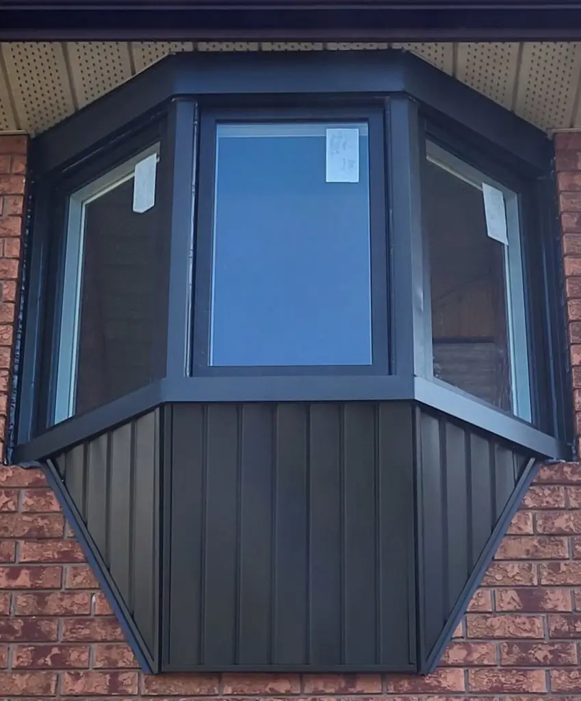 NTI Windows & Doors A black-framed bay window from GTA Windows with three glass panels extends outward from a brick building. White stickers are visible on the window glass. Window Replacement Hamilton & GTA
