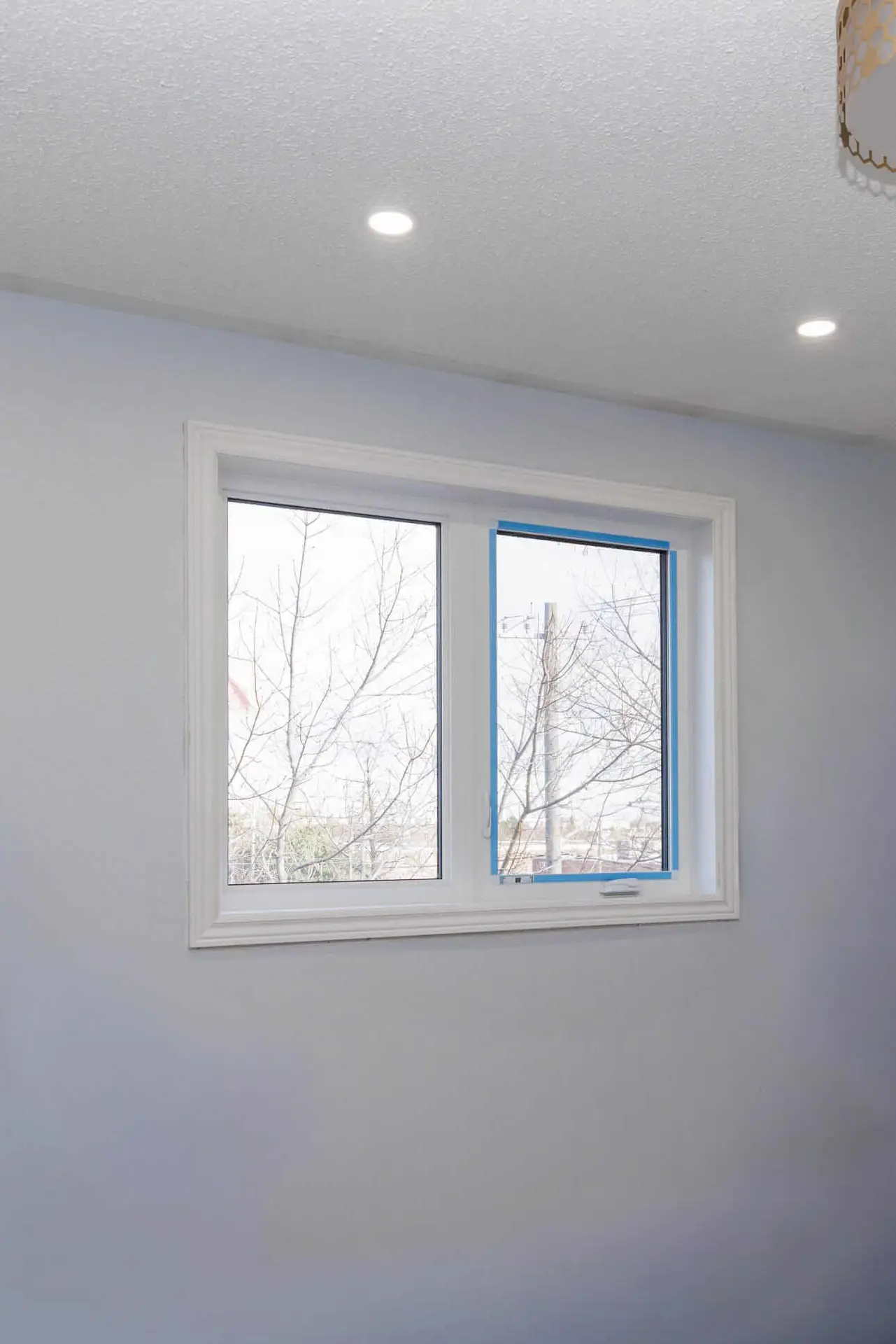 NTI Windows & Doors A double-paned GTA Windows installation set in a white wall, with one pane slightly open and blue painter’s tape on the frame; leafless trees are visible outside. Window Replacement Hamilton & GTA